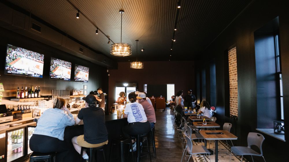 The slick, black interior of Proximity Brewing in East Durham. Customers fill the bar seats.