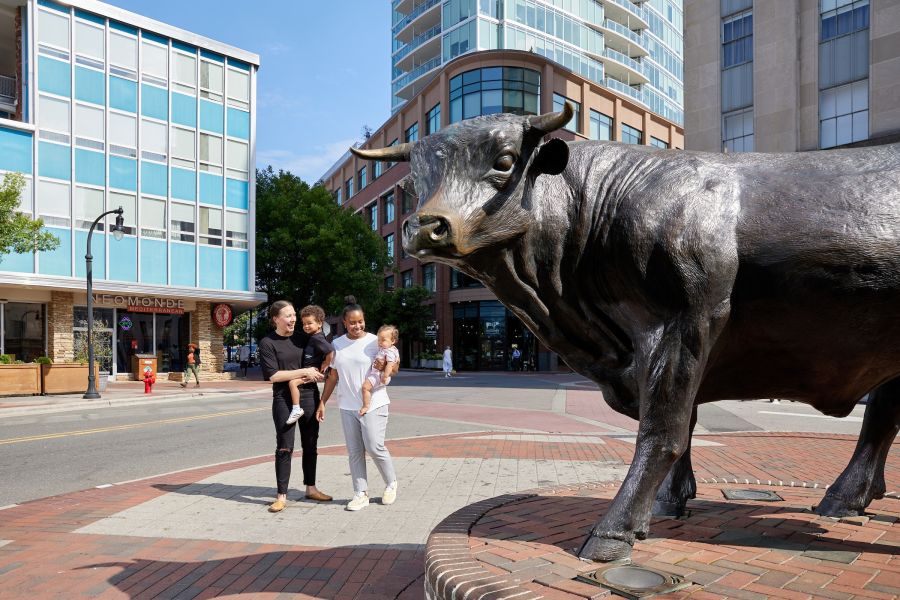 A family walks by Major the Bull in downtown Durham on a sunny day.